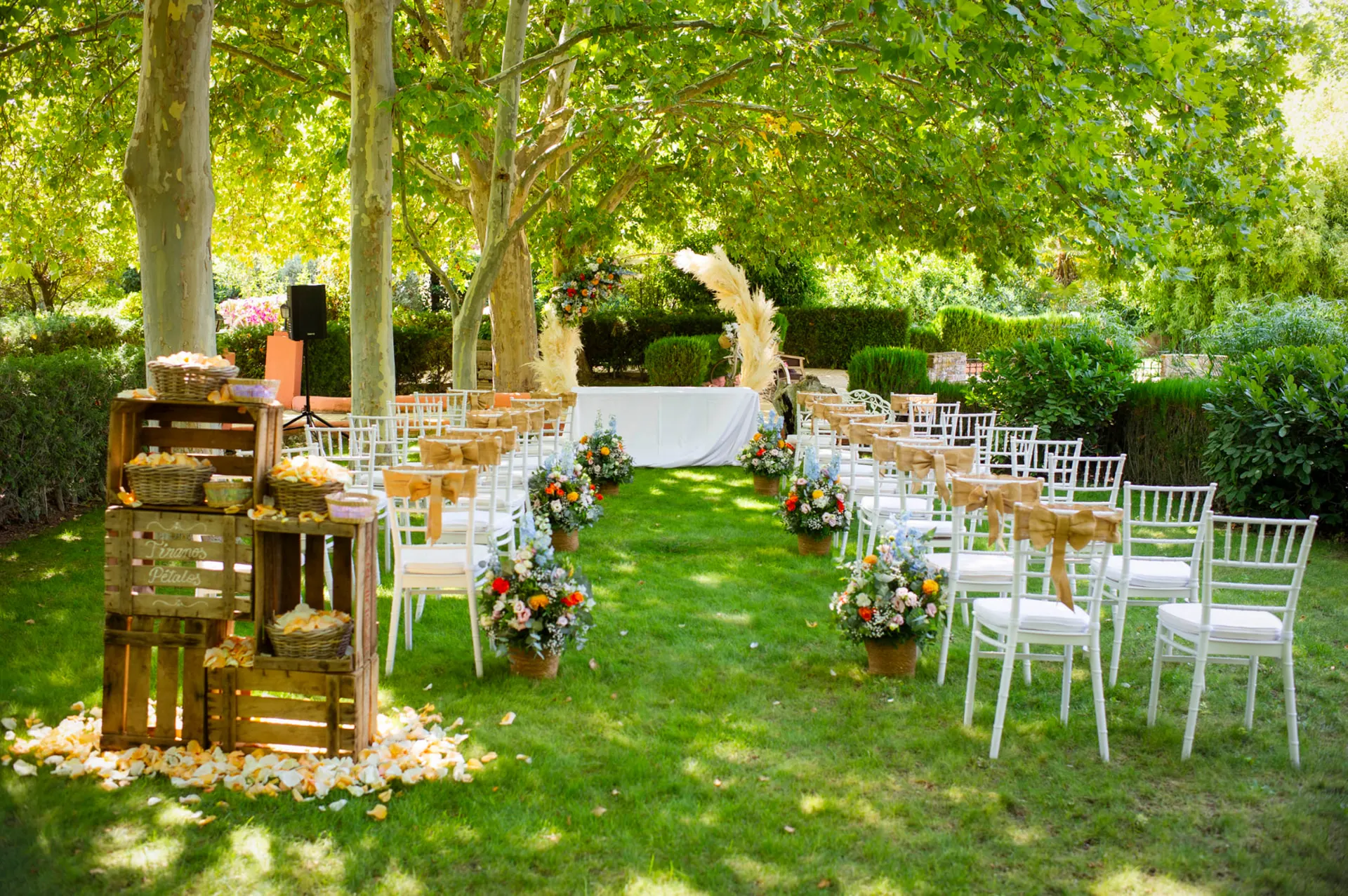 Ceremonia al aire libre con sillas blancas, pétalos y altar floral bajo los árboles en Finca La Peraleña