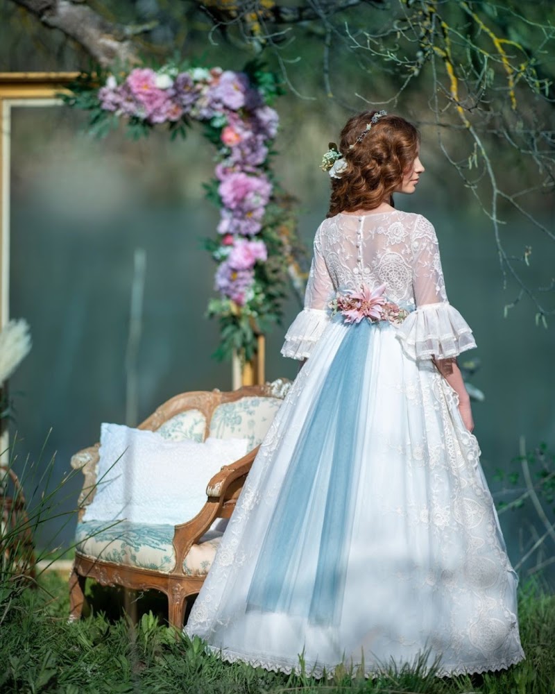 Niña vestida de comunión con vestido de encaje y detalle floral, vista de espaldas en un entorno natural