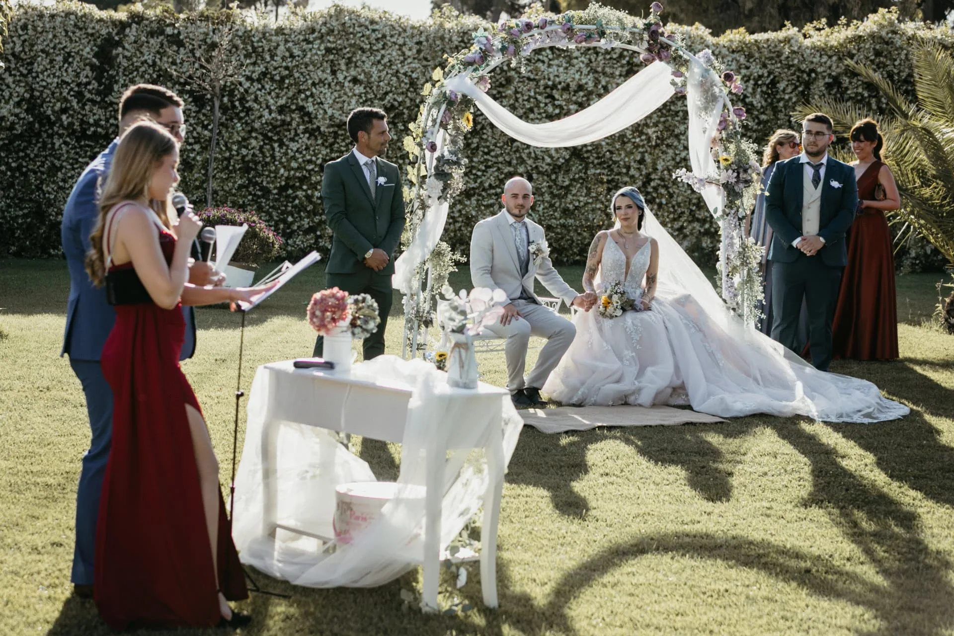 Ceremonia de boda al aire libre con arco floral y los novios sentados en el jardín